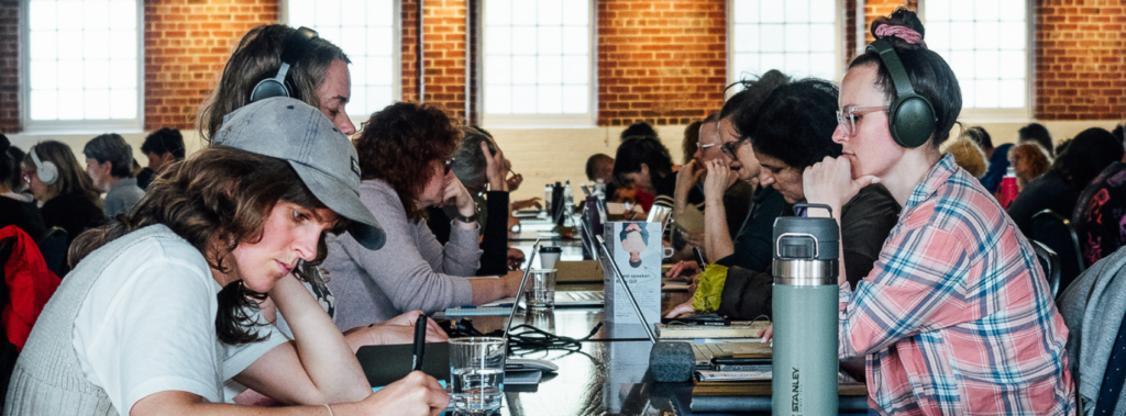 A lot of people sitting in a beautiful old brick hall writing at tables.