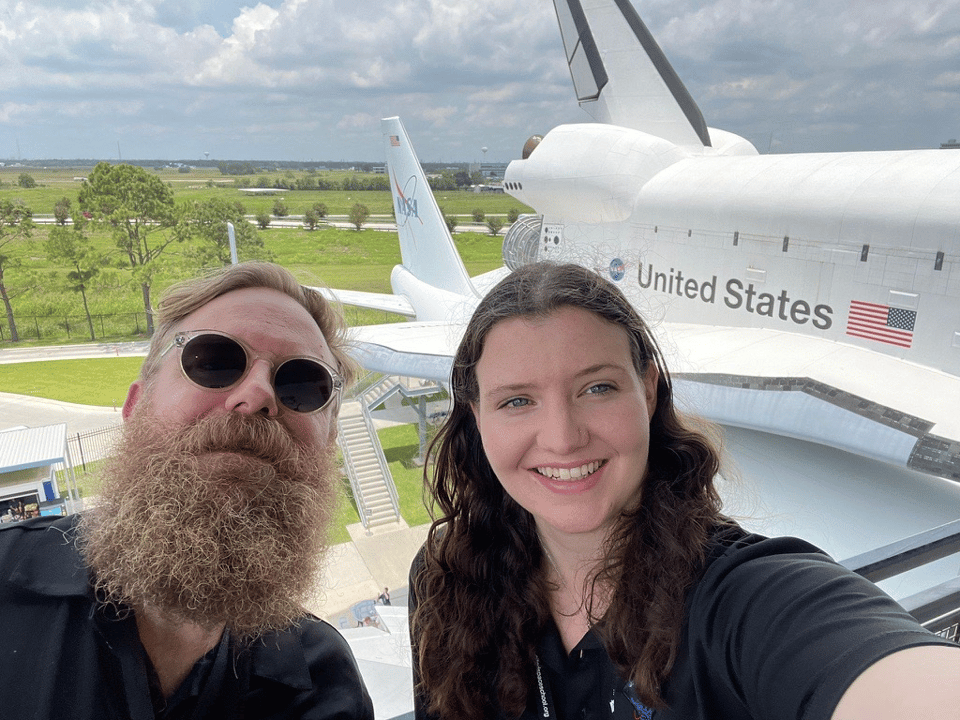 A very beardy and sweaty JJW and Tori pose for a photo with the tail end of the replica shuttle and Boeing 747 in the background.