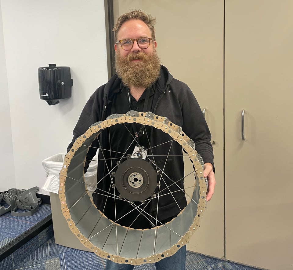 JJW is holding a prototype wheel that will be used on the VIPER rover.